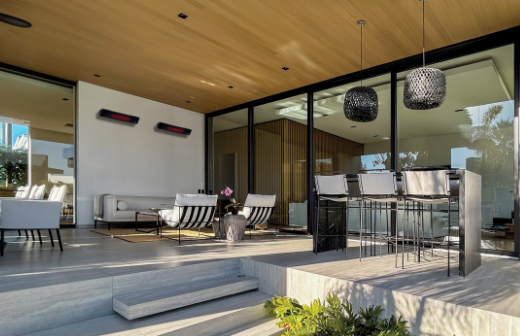 Modern outdoor living space with furniture and glass walls. Two Rio Patio heaters on back wall.