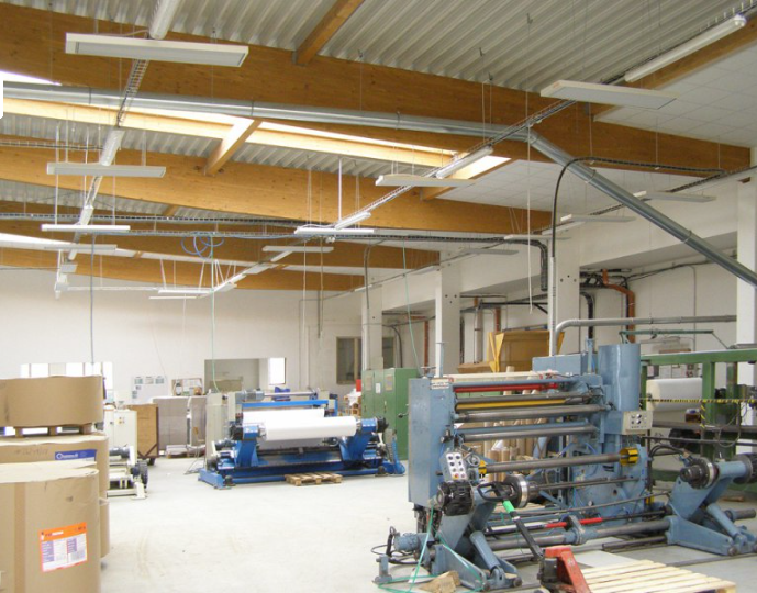 Factory interior with large industrial machines and equipment as well as large heaters hanging from the ceiling