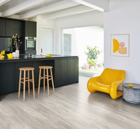 Modern kitchen with black island, wooden stools, and a yellow chair and Oak-Nordic-grey flooring 