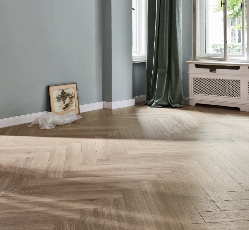 Herringbone wooden floor with a radiator and window in a room with gray walls.