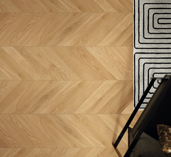 Wooden floor with a chevron pattern and a part of a rug with geometric design.