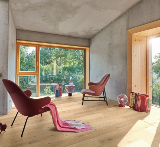 Modern interior with pink chairs and a rug on Oak Natural Mix light  Vinyl Chalet Classic 2070 Wide plank, large windows showing greenery outside.