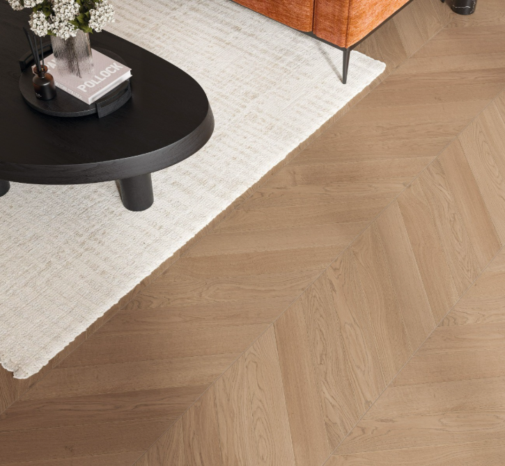 Wooden floor with chevron pattern, black round table, and white rug.