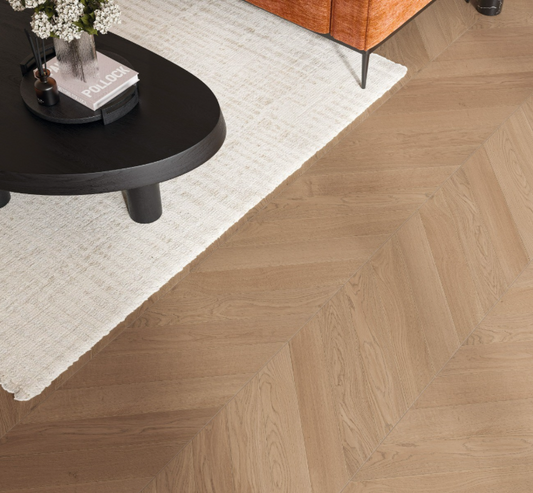Wooden floor with chevron pattern, black round table, and white rug.