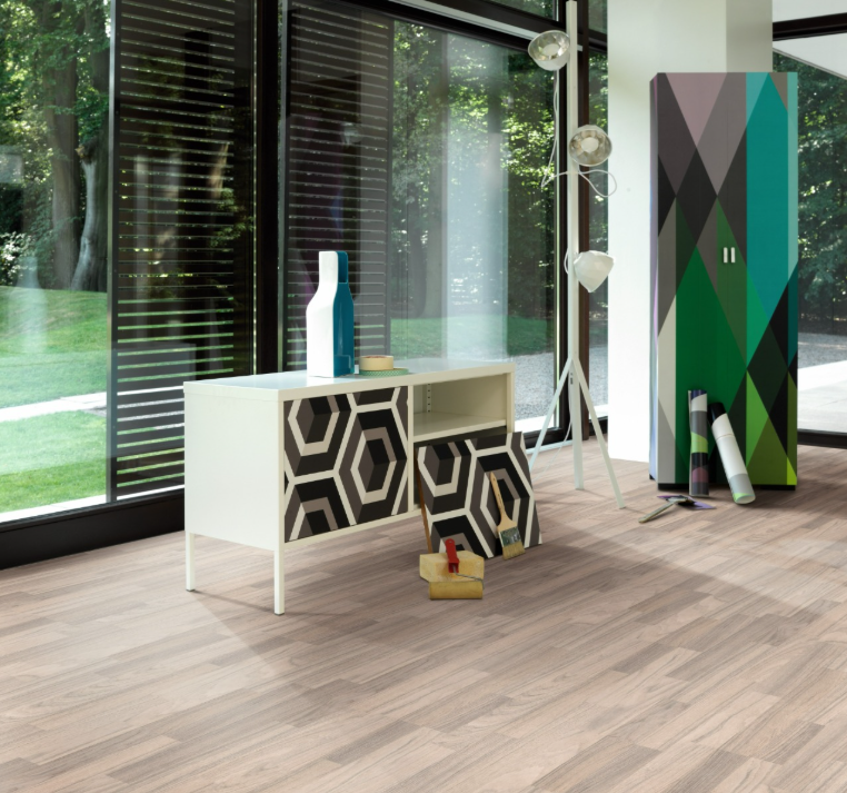 A room showcasing laminate flooring with a teak wood appearance, featuring a modern white cabinet, decorative items, and large windows with a outdoor view.