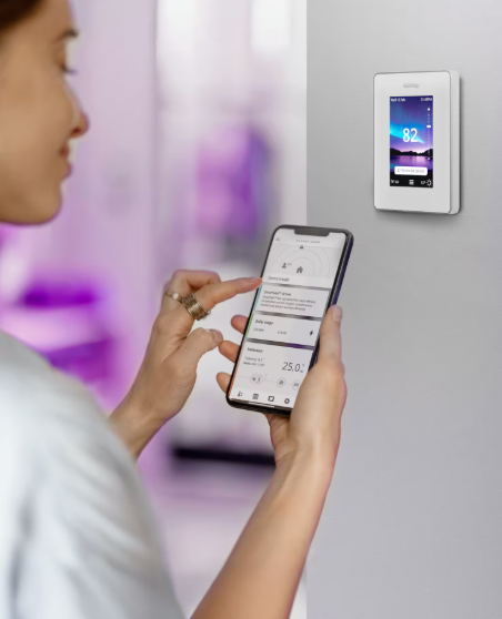 Person using a smartphone to control a smart thermostat on a wall.