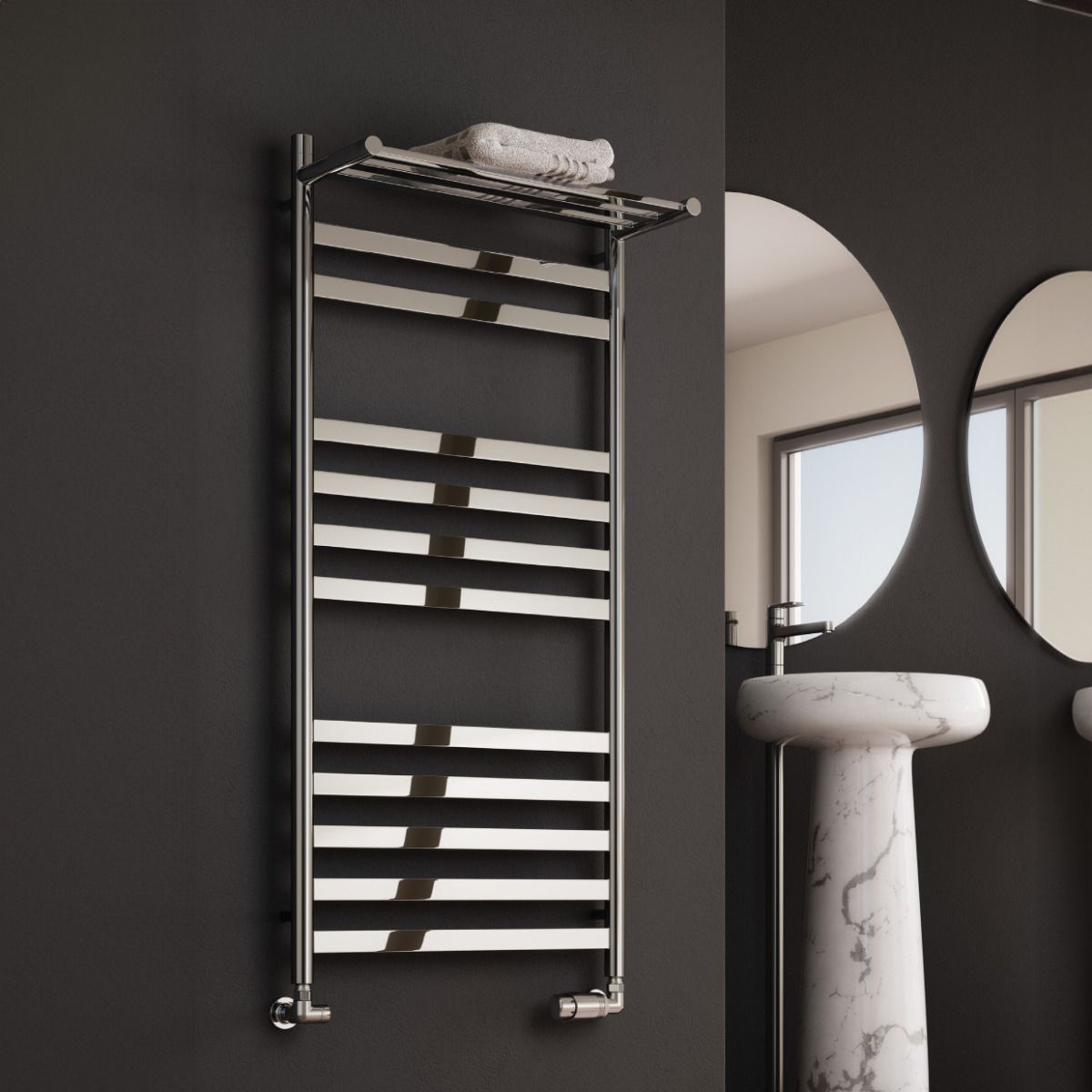 Towel radiator mounted on a dark wall with a bathroom setting including a sink and mirrors.