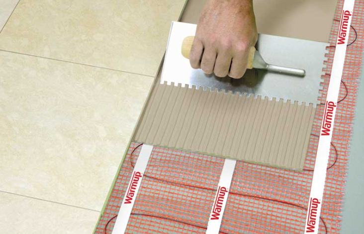 Professional installer laying Warmup StickyMat electric underfloor heating system onto a prepared subfloor prior to tiling.